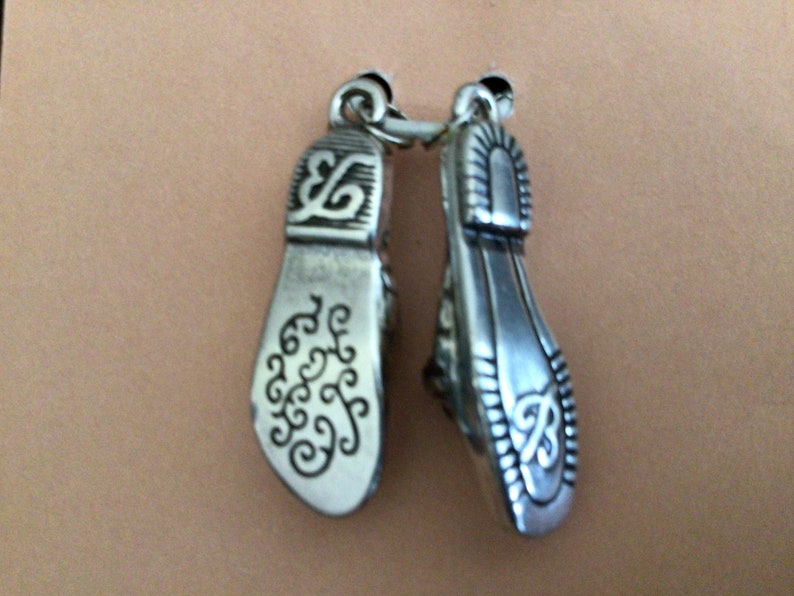Pode incluir: Um par de pingentes de prata em forma de sapatos com desenhos florais intrincados.