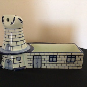 May include: A ceramic holder shaped like a building with an attached tower, featuring a light cream base color with hand-painted dark blue outlines depicting brick patterns, windows, and doors. The structure includes an open rectangular tray.