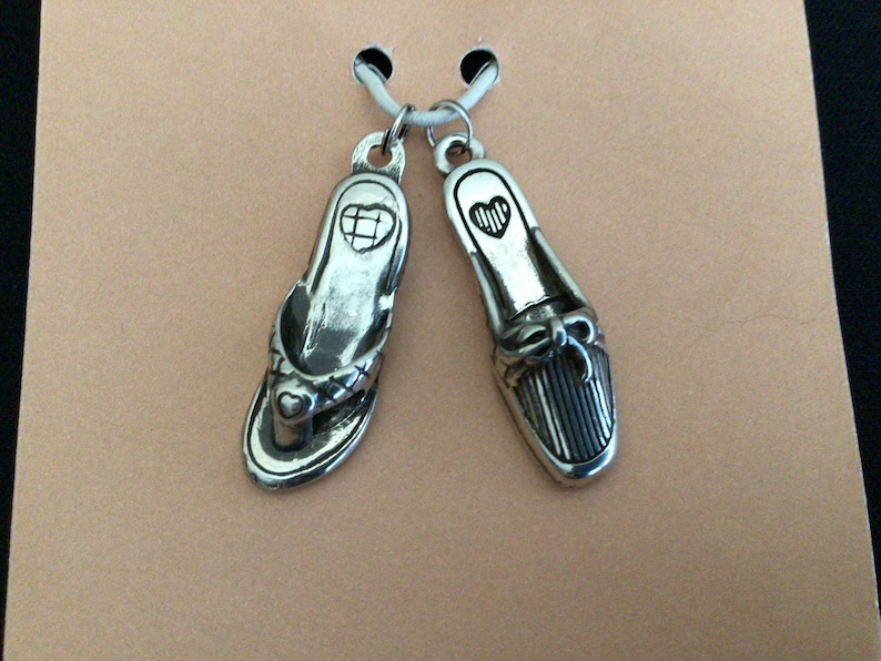 Pode incluir: Um par de pingentes de prata em forma de chinelo e sapato de salto alto. Ambos os pingentes t&ecirc;m um pequeno cora&ccedil;&atilde;o gravado.