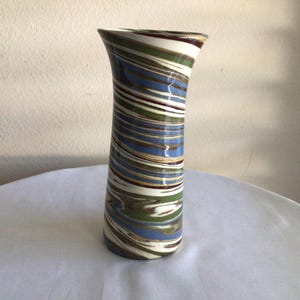 May include: A tall, ceramic vase with a swirling pattern of blue, green, white, and brown stripes. The vase has a flared top and a cylindrical body. Decorative home decor item.