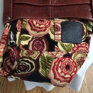 May include: A brown leather handbag with a floral patterned interior. The bag features a textured exterior and a silver-colored clasp. The interior fabric displays a pattern of red, pink, and cream-colored flowers on a black background.