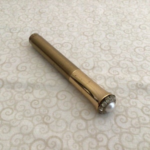 May include: A gold-colored metal pen with a pearl-like top accented with rhinestones.
