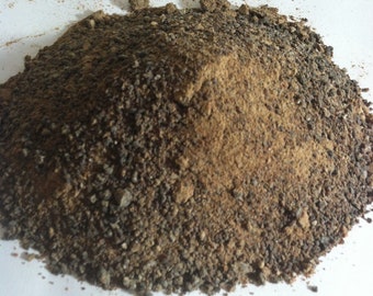 Puede incluir: Un montón de material granular grueso que presenta una mezcla de partículas de color marrón oscuro, bronceado y negro. La textura es irregular, compuesta por pequeñas piezas desiguales y granos finos apilados en forma cónica sobre una superficie.