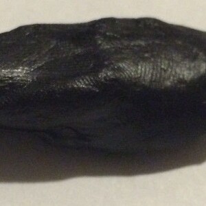 May include: A smooth, black, oval-shaped rock with a textured surface.