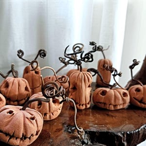 May include: A group of carved orange pumpkins with detailed faces and curly stems. The pumpkins are displayed on a dark wooden surface, creating a festive Halloween scene. The background features a white curtain.