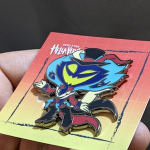 May include: A silver and black enamel pin featuring a cartoon character with blue hair, a yellow face, and a red cape. The pin is on a card with the text "Into the Hellaverse".