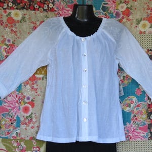 May include: A white, semi-sheer, long-sleeved blouse with a button-up front and a gathered neckline.