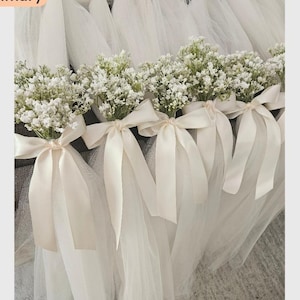 May include: Several small bouquets of white flowers tied with ivory satin ribbons and tulle. The bouquets are arranged in a row, with the tulle cascading down. The flowers are a delicate accent for weddings or other special events.