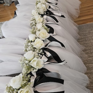 May include: White tulle table skirt with black and white ribbon bows and white roses with greenery.