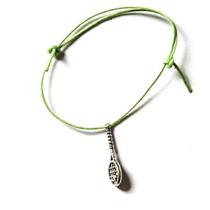Puede incluir: Un brazalete de cuerda verde con un dije de raqueta de tenis plateado.