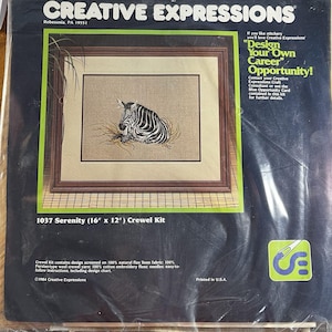 May include: A crewel embroidery kit titled "Serenity" featuring a framed zebra design. The kit includes natural flax linen fabric, wool yarn, cotton embroidery floss, and needles. The package is labeled "Creative Expressions" and measures 16" x 12".