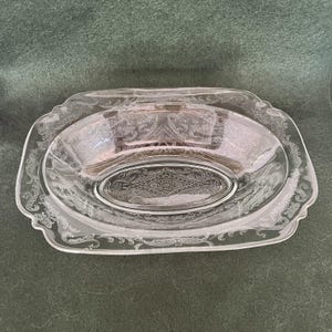 May include: Clear glass serving dish with an oval center and a decorative, etched paisley design. The dish has a rectangular shape with scalloped edges. The glass is transparent, allowing light to pass through, and is suitable for serving food.