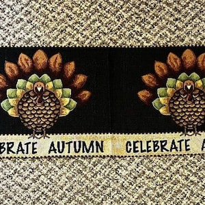 May include: A black fabric table runner with four turkeys and the text "Celebrate Autumn" repeated four times. The turkeys are brown, green, and gold with a black background.