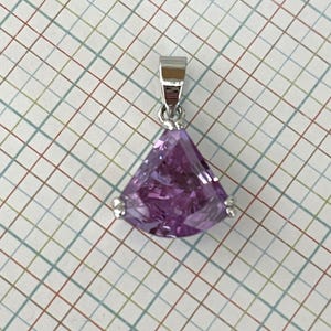 May include: A silver pendant with a triangular, faceted, purple gemstone. The pendant has a small silver bail at the top for a chain. The gemstone is a vibrant shade of purple and is set in a silver setting.