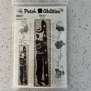 May include: A clear plastic package containing a fabric applique pattern. The pattern features a skier design with a hat, scarf, and skis. The text "Skier" and "6"x24"" are visible. The package also includes the text "Patch Abilities" and "MM01".