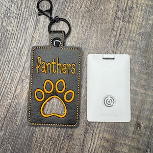 May include: Black rectangular keychain with the word "Panthers" in gold lettering and a gold paw print. The keychain has a black metal clasp and a white rectangular card with the word "CENTEGIX" printed on it.