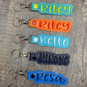 May include: Seven colorful leather keychains with metal rings and clasps. Each keychain has a different name embroidered on it: Jessica, Riley, Belle, Tyrone, Resa, and Helen.