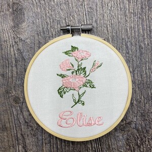 May include: Embroidered hoop with a pink floral design and the name "Elise" in pink thread.