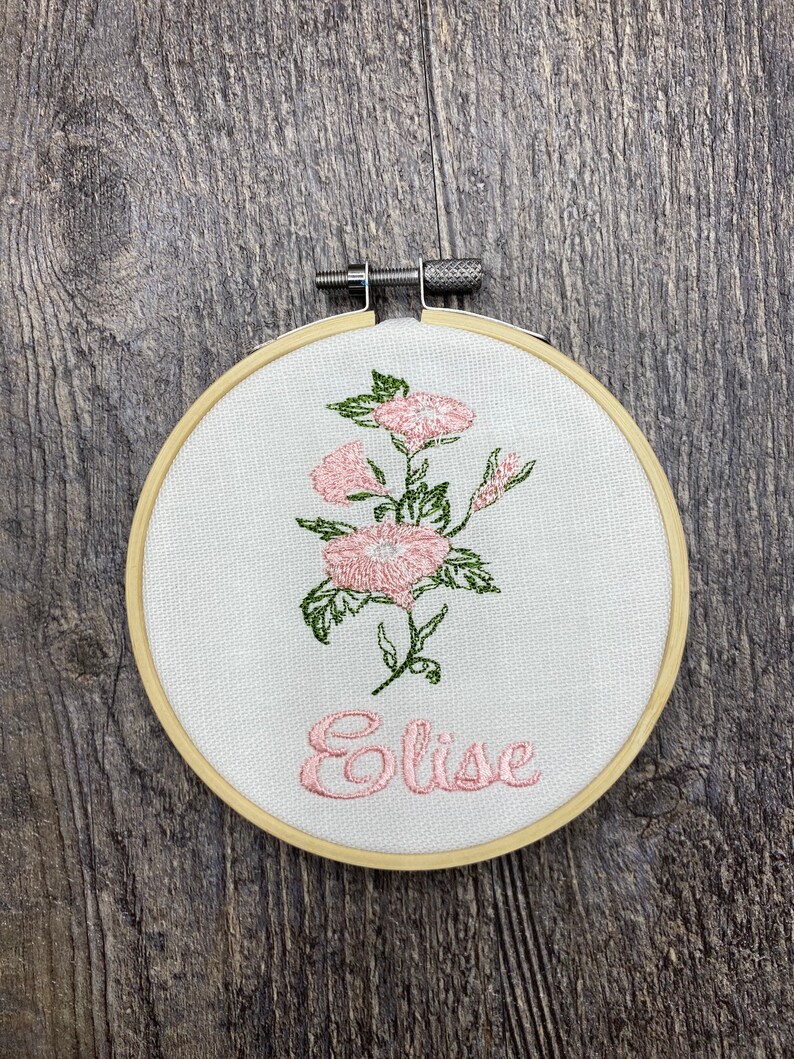 May include: Embroidered hoop with a pink floral design and the name "Elise" in pink thread.