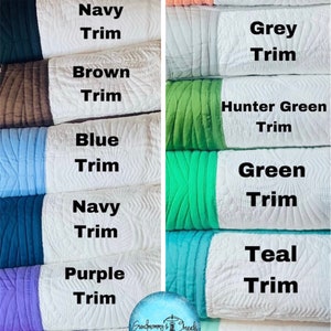 K&ouml;nnte beinhalten: Ein Stapel gesteppter Stoffquadrate mit verschiedenen farbigen Einfassungen. Die Farben umfassen Rosa, Wei&szlig;, Marineblau, Braun, Blau, Gr&uuml;n, T&uuml;rkis, Mint, Koralle, Grau und Huntergr&uuml;n. Die Stoffquadrate sind alle wei&szlig; mit einer andersfarbigen Einfassung auf der linken Seite jedes Quadrats. Der Text "Grandma's Threads" ist auf dem unteren linken Quadrat sichtbar.