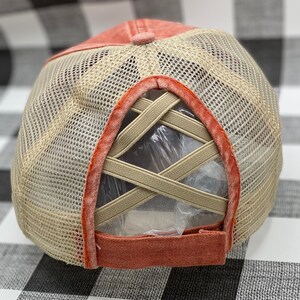 May include: A coral colored mesh baseball cap with a criss-cross elastic band in the back.