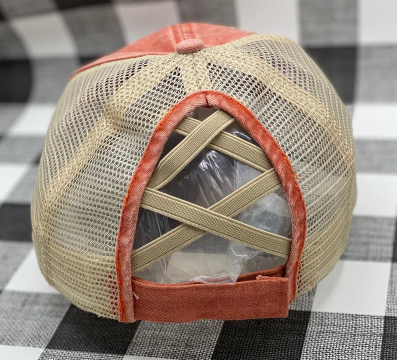 May include: A coral colored mesh baseball cap with a criss-cross elastic band in the back.