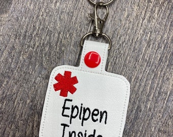May include: White keychain with a red medical symbol and the text "Epipen Inside".