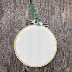 May include: A white embroidery hoop with a green string attached to it. The hoop is hanging on a wooden surface.
