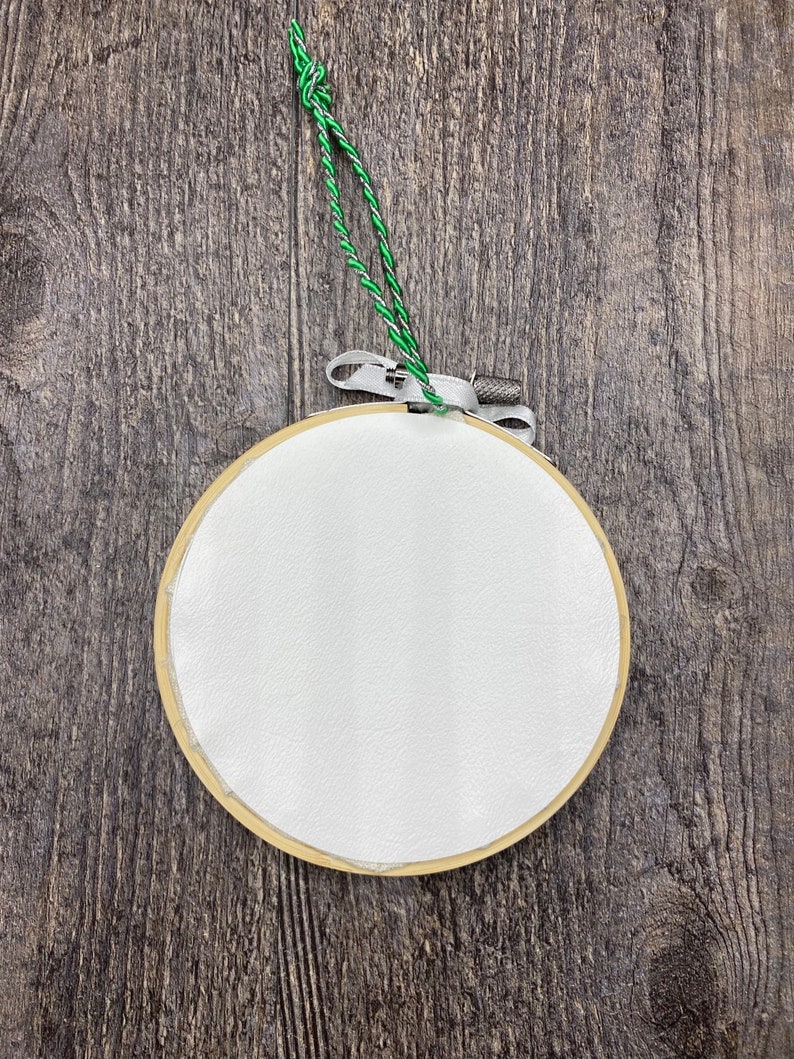 May include: A white embroidery hoop with a green string attached to it. The hoop is hanging on a wooden surface.