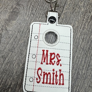 May include: White key chain with a paper-like design and a red embroidered name "Mrs. Smith".