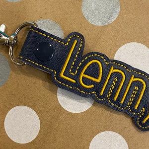 May include: A dark blue leather keychain with a yellow embroidered name "Lenny" and a silver key ring.