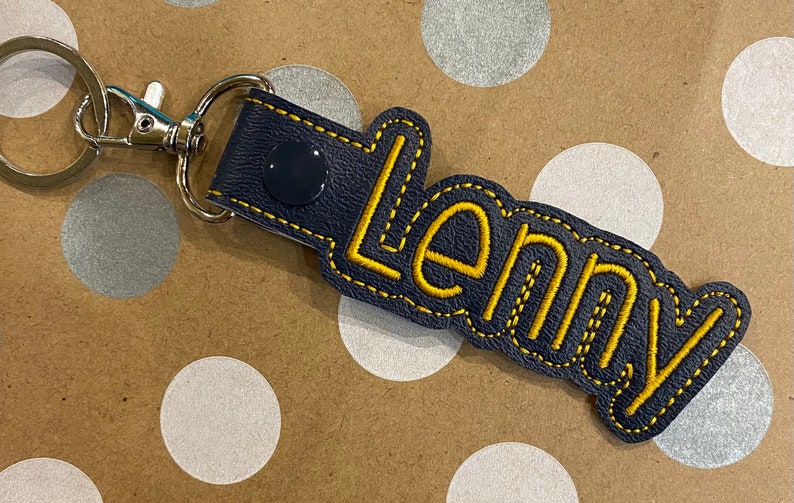 May include: A dark blue leather keychain with a yellow embroidered name "Lenny" and a silver key ring.