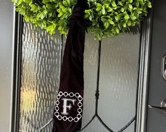May include: A black velvet stocking with a white embroidered letter "F" in a circle design. The stocking is hanging on a door with a green wreath.