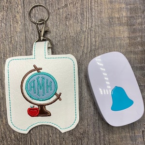 May include: White leather keychain with a blue and brown globe design and the monogram "AMH". A small white bell with a blue button is also pictured.