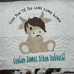 May include: A white quilted baby blanket with a brown cow applique and the text "Love You 'til the cows come home" and "Cohen James Dixon Rubrecht" embroidered in green thread.