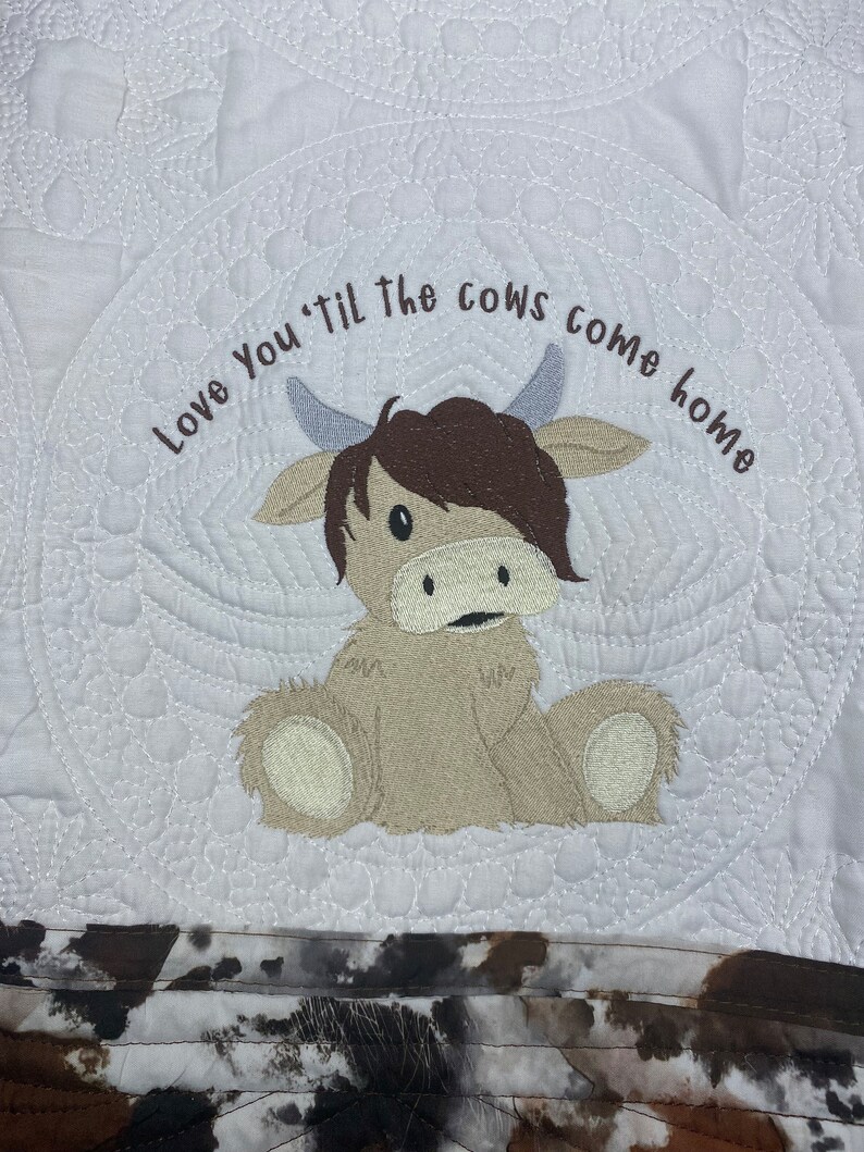 May include: White quilted fabric with a brown and white cow applique and the text "Love You 'til the cows come home".