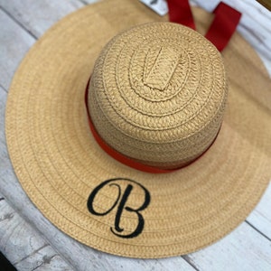 May include: A straw sun hat with a red ribbon and the initials "OB" embroidered on the front.