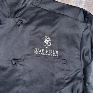 May include: Black chef jacket with a white embroidered logo that says "LUXE POUR WINE ACCESSORIES".