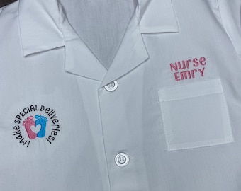 Puede incluir: Bata blanca de laboratorio con un bolsillo bordado en rosa en el lado derecho que dice "NURSE EMRY". El lado izquierdo tiene un círculo bordado en negro con el texto "I make SPECIAL DELIVERIES" y un diseño de huella de pie rosa y azul.