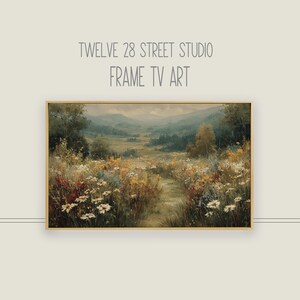 Puede incluir: Pintura de paisaje enmarcada que representa un camino a través de un campo de flores silvestres, que conduce a una cordillera. La obra de arte tiene un marco dorado y el texto "TWELVE 28 STREET STUDIO FRAME TV ART" en la parte superior.