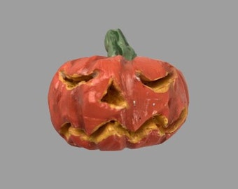 Può includere: Una piccola zucca arancione con un viso di zucca intagliato. La zucca ha un gambo verde e una superficie testurizzata.