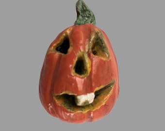Può includere: Una zucca in ceramica dipinta a mano con un viso di zucca intagliato. La zucca è arancione con uno stelo verde e occhi, naso e bocca neri.