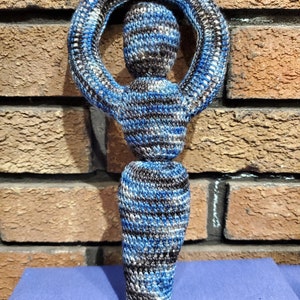 May include: A crocheted figure with a blue, black, and white striped pattern. The figure has a circle around its head and a long, flowing skirt.