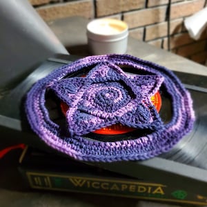 May include: A purple and blue crocheted star with a white center. The star is lying on a black record player.