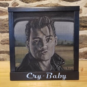 May include: A black framed screen print of a man's face with the text "Cry-Baby" below the image.