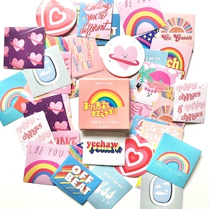 May include: A selection of stickers and cards featuring a variety of designs. The designs include rainbows, hearts, and phrases like "Be You" and "Yeehaw". The color scheme is predominantly pastel shades with accents of vibrant hues.