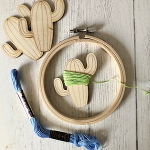 May include: A wooden cactus embroidery hoop kit with light green embroidery floss and a blue embroidery floss skein. The kit includes a wooden cactus cutout and a wooden embroidery hoop.