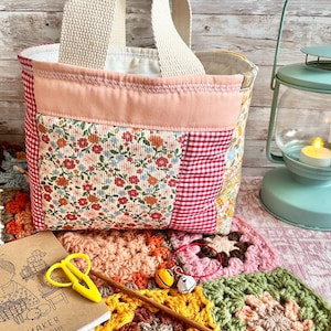 May include: A quilted fabric tote bag featuring a patchwork design of red and white gingham, floral patterns, and a solid peach-coloured top band with cream-coloured woven handles. The bag is constructed with visible stitching and a light-coloured interior lining.