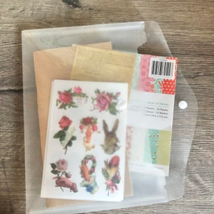 May include: A clear plastic envelope containing a set of 36 paper stickers with floral and animal designs. The stickers are on white sheets and feature images of roses, a rabbit, and a hand holding a wreath. The envelope also contains two sheets of patterned paper with a variety of colours and designs. The envelope has a label that reads "Bloc de Papel" and includes the text "Papiens 36 Papeles, Conçoit 24 Diseños, 5 in (15.2 x 15.2 cm)".