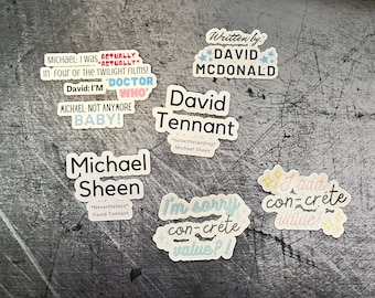 May include: A collection of stickers with text and illustrations. The stickers are on a gray background. The text on the stickers includes "I was actually in four of the Twilight films!" "David: I'm Doctor Who" "Michael not anymore baby!" "Written by: David McDonald" "David Tennant" "notwithstanding Michael Sheen" "I add concrete value!" "I'm sorry concrete value?!" "Michael Sheen" "Nevertheless David Tennant"